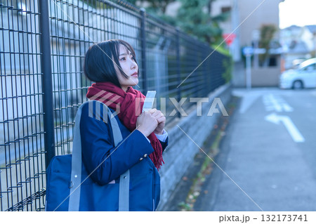 寒い日に部活で登下校する女子高生　冬服でカイロを持ち友達を待つ高校生　登校下校　 132173741