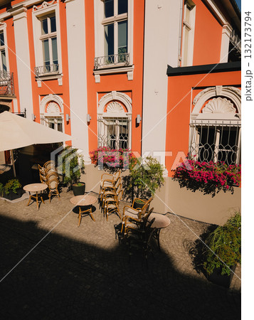 Quaint outdoor cafe setting with stacked chairs, round tables, flowering window boxes adorning historic building, evoking peaceful European street ambiance. Cozy outdoor cafe. Cute European atmosphere Quaint outdoor cafe setting with stacked chairs, round tables, flowering window boxes adorning historic building, evoking peaceful European street ambiance. Cozy outdoor cafe. Cute European atmosphere 132173794