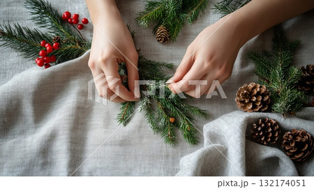 Hands arranging pine branches and berries for Christmas decoration on fabric background. Christmas decor and craftwork, eco friendly, sustainable concept. Hands arranging pine branches and berries for Christmas decoration on fabric background. Christmas decor and craftwork, eco friendly, sustainable concept. 132174051