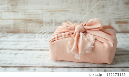 Wrapped Christmas gift in peach fabric, set against a rustic wooden backdrop. Japanese Furoshiki style, eco friendly, environmental gift wrapping concept. Place for text. Wrapped Christmas gift in peach fabric, set against a rustic wooden backdrop. Japanese Furoshiki style, eco friendly, environmental gift wrapping concept. Place for text. 132175183