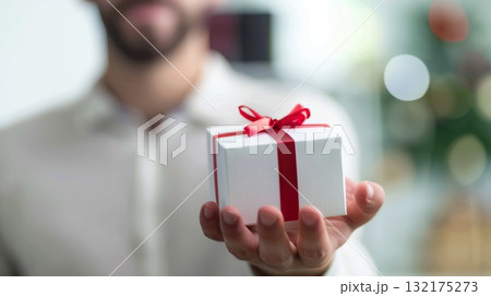 Male holding a small gift with an red bow. Christmas gift. Congratulation. 132175273