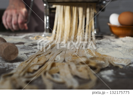 Caucasian female hands making fettuccine noodles using mechanical pasta machine 132175775