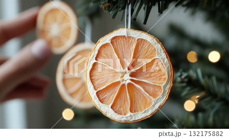 Hand placing dried orange slices on a green Christmas tree. Eco-friendly holiday decor, sustainable, holiday decor concept 132175882