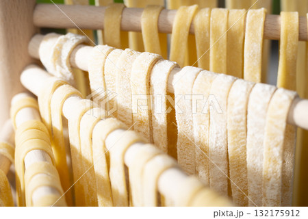 Homemade noodles hanging on wooden dryer rack closeup low angle view Homemade noodles hanging on wooden dryer rack closeup low angle view 132175912