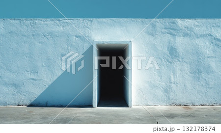 Minimalist Blue Wall With Dark Entrance Doorway and Sharp Shadow in Sunlit Exterior 132178374