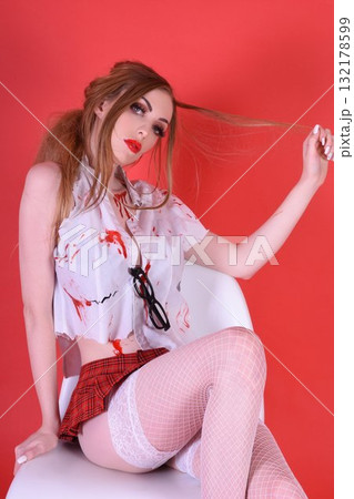 Shapely, redhead model dressed as a Zombie Schoolgirl for Halloween, isolated against a red background Shapely, redhead model dressed as a Zombie Schoolgirl for Halloween, isolated against a red background 132178599
