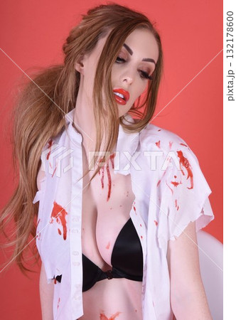 Shapely, redhead model dressed as a Zombie Schoolgirl for Halloween, isolated against a red background 132178600
