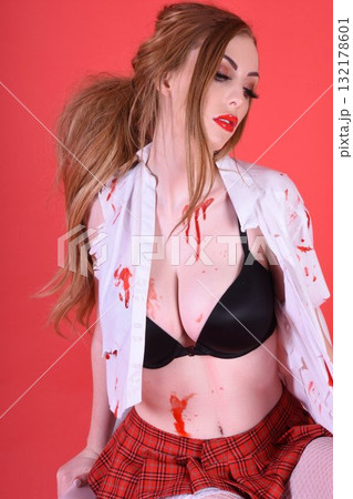 Shapely, redhead model dressed as a Zombie Schoolgirl for Halloween, isolated against a red background Shapely, redhead model dressed as a Zombie Schoolgirl for Halloween, isolated against a red background 132178601