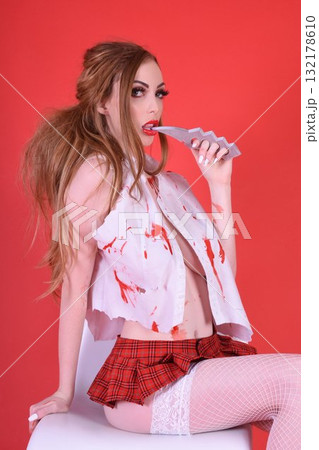 Shapely, redhead model dressed as a Zombie Schoolgirl for Halloween, isolated against a red background 132178610