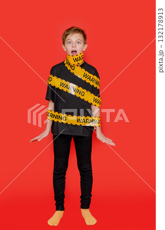 Boy stands with yellow warning tape wrapped around his body and mouth 132178913