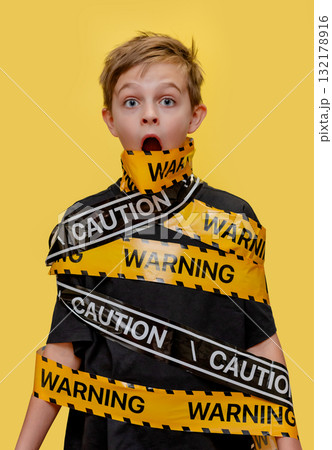 Boy stands with yellow warning tape wrapped around his body and mouth, 132178916