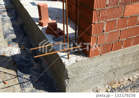 A construction site features a newly built brick wall with visible rebar bars extending from the concrete foundation. A construction site features a newly built brick wall with visible rebar bars extending from the concrete foundation. 132179256