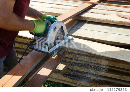 A worker saws wooden planks with a circular saw in a green, sunny place. 132179258