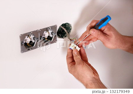 A person is engaged in an electrical repair task at home, carefully working with wires and tools near a wall outlet. 132179349