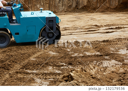 Blue roller compacts the ground on freshly dug soil at a construction site installed 132179536