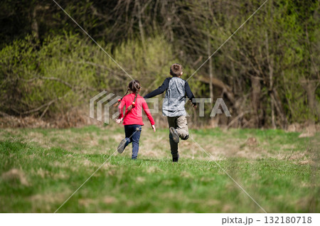 Two children run through a sunny field, enjoying a carefree day outdoors. 132180718