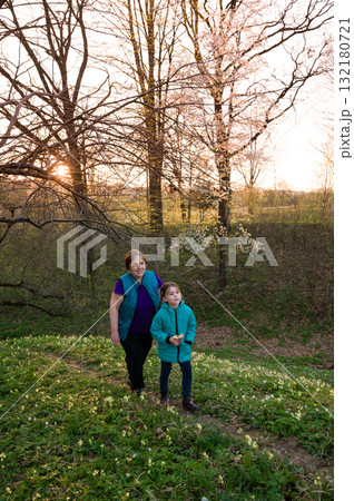 Grandmother and granddaughter enjoy a springtime walk through a blooming park, bathed in the golden light of sunset. 132180721