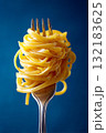 Close up studio photograph of a fork holding neatly twirled pasta against a vibrant blue background 132183625