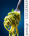 Close up of a fork with spaghetti strands and fresh herbs on a vibrant blue background 132183629