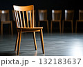 Empty wooden chair positioned alone in a dimly lit room, symbolizing isolation and exclusion 132183637