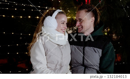 Young couple embracing, sharing tender moment amid softly glowing christmas lights, radiating love and warmth during holiday celebration 132184013