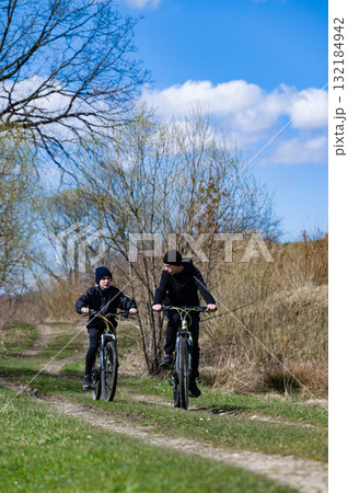 Two cyclists enjoy a sunny day riding mountain bikes on a dirt trail through a scenic landscape. 132184942