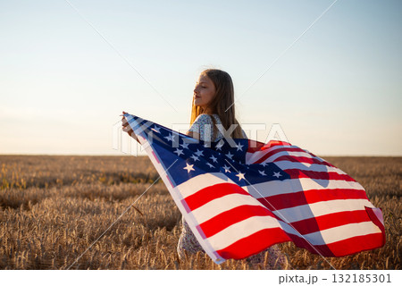 Girl in the field with flag of USA. American girl in ripe field of rye or wheat in the evening Girl in the field with flag of USA. American girl in ripe field of rye or wheat in the evening 132185301