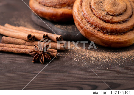 Cinnamon buns on black wooden table. Cinnamon sticks and anise stars near buns Cinnamon buns on black wooden table. Cinnamon sticks and anise stars near buns 132185306