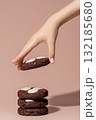 Hand reaching for chocolate cookies with white chocolate chips on a soft pastel background with copy space 132185680