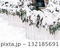 Snow-covered white fence adorned with evergreen garlands and twinkling lights for Christmas ambiance 132185691