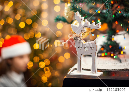 Wooden deer as Christmas symbol standing on the piano, atmosphere of the holidays. Bright lights, festive decoration and female pianist on the background. 132185905