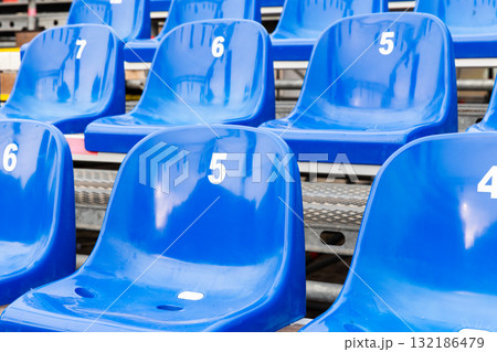 Vivid blue plastic stadium seats numbered 5, 6, and 7 sit in an empty grandstand Vivid blue plastic stadium seats numbered 5, 6, and 7 sit in an empty grandstand 132186479