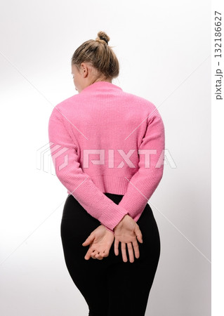 Woman in pink sweater and black leggings, hands behind back, facing away. Woman in pink sweater and black leggings, hands behind back, facing away. 132186627