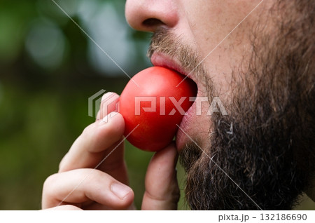 Man eating a ripe red fruit outdoors 132186690
