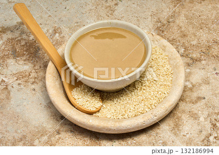 Sesame Tahini Bowl. A bowl of creamy tahini with sesame seeds on a rustic travertine surface. 132186994