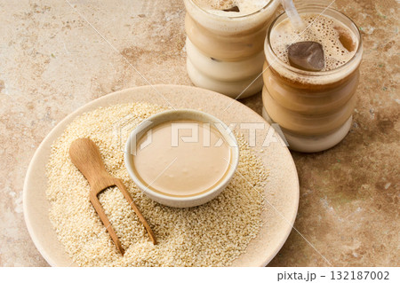 Sesame Tahini Latte Delight. Creamy sesame paste and iced tahini lattes on rustic travertine surface. 132187002