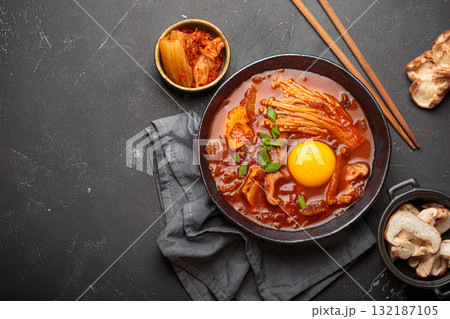 Traditional Korean kimchi jjigae hot soup or stew with egg yolk in black rustic bowl on dark background top view, space for text 132187105