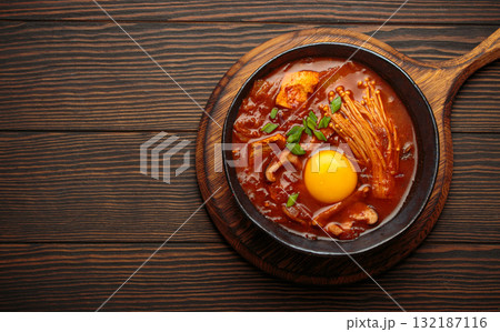 Traditional Korean kimchi jjigae hot soup or stew with egg yolk in black rustic bowl on dark wooden background top view, space for text Traditional Korean kimchi jjigae hot soup or stew with egg yolk in black rustic bowl on dark wooden background top view, space for text 132187116