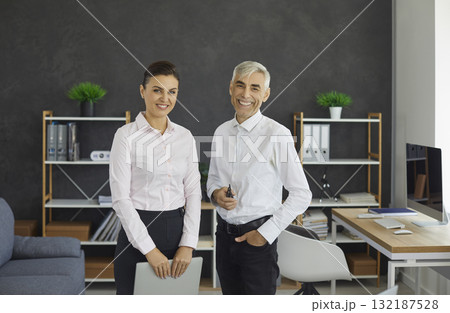 Senior male boss and young female secretary standing in office portrait 132187528