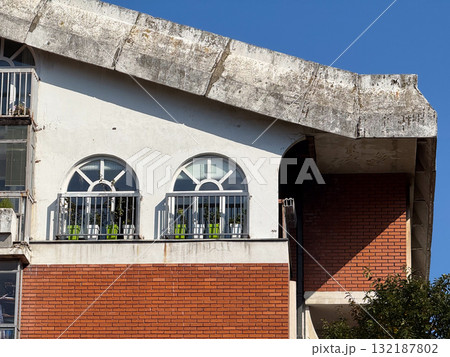 Modern residential building with red brick wall and white arched windows under blue sky. Urban design, architecture, and combination of geometric shapes in sunlight. Modern residential building with red brick wall and white arched windows under blue sky. Urban design, architecture, and combination of geometric shapes in sunlight. 132187802