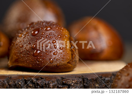 a hard edible chestnut fruit in a brown shell covered with water droplets on a wooden table, a group of wet fruits with a brown hard shell a hard edible chestnut fruit in a brown shell covered with water droplets on a wooden table, a group of wet fruits with a brown hard shell 132187860