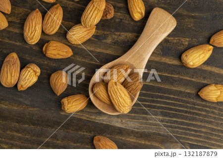 yellow brown whole nuts of almonds with a wooden spoon on the table, a large number of hard raw almonds on the table during cooking yellow brown whole nuts of almonds with a wooden spoon on the table, a large number of hard raw almonds on the table during cooking 132187879
