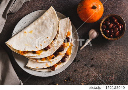 Delicious tacos with baked pumpkin, beans and cheese on a plate on the table top view Delicious tacos with baked pumpkin, beans and cheese on a plate on the table top view 132188040