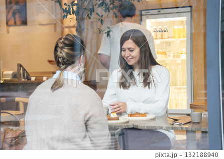 Two women sit inside ABC Coffee cafe in Moscow, talking over coffee and pastries, seen through the window Two women sit inside ABC Coffee cafe in Moscow, talking over coffee and pastries, seen through the window 132188940