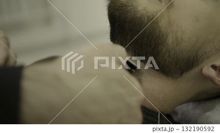 Professional barber trimming man's beard with electric razor. Clip 132190592