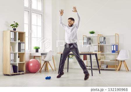 Happy young business man doing star jumps during a fitness workout in the office Happy young business man doing star jumps during a fitness workout in the office 132190968