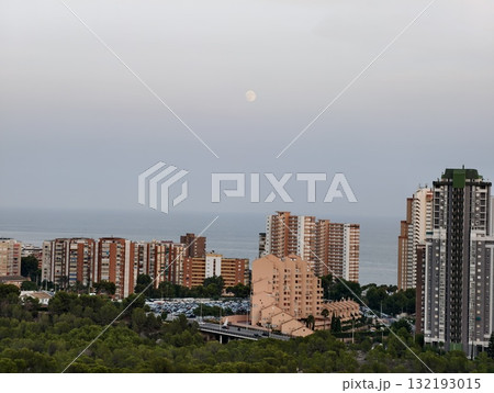 A Serene Cityscape at Dusk with the Majestic Moon Gracefully Overlooking the Calm Sea 132193015