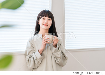 窓辺でホットドリンク,お茶,コーヒーを飲見ながらスマホを見る若いアジア人女性 窓辺でホットドリンク,お茶,コーヒーを飲見ながらスマホを見る若いアジア人女性 132193059
