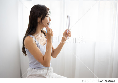 手鏡を持って歯磨きをする若い女性 手鏡を持って歯磨きをする若い女性 132193088