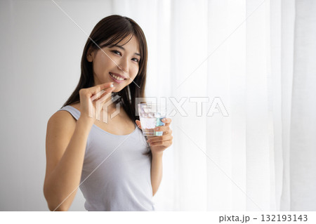 窓辺でサプリメントの錠剤を飲む若い女性 132193143